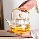 Chaleira de vidro 1L com infusor e alça de bambu natural, servida com chá em ambiente aconchegante - Casa Splêndida