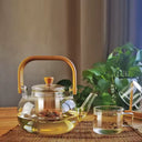 Chaleira de vidro 1L com infusor e alça de bambu natural, servida com chá em ambiente aconchegante - Casa Splêndida