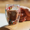 Caneca de vidro duplo com flores secas coloridas e bebida quente sendo servida - Casa Splêndida