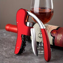 Abridor de Vinho e Saca-Rolhas com Alavanca Premium Casa Splendida vermelho ao lado de uma taça de vinho, exibindo sofisticação na mesa.