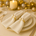 Anéis para guardanapo com pérola dupla dourada em mesa posta elegante, com guardanapos claros e iluminação quente, estilo sofisticado Casa Splendida
