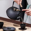 Chaleira japonesa preta de ferro fundido Casa Splendida servindo chá em xícara combinando sobre mesa rústica