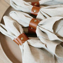 Porta‑guardanapo de couro marrom com rebite metálico em mesa posta estilo farmhouse, conjunto com guardanapos claros