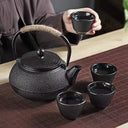 Chaleira japonesa preta de ferro fundido Casa Splendida servindo chá em xícara combinando sobre mesa rústica