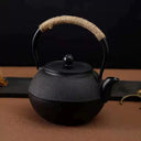 Chaleira japonesa preta de ferro fundido Casa Splendida servindo chá em xícara combinando sobre mesa rústica