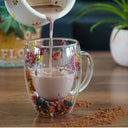 Caneca de vidro duplo com flores secas coloridas e bebida quente sendo servida - Casa Splêndida