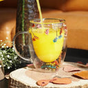 Caneca de vidro duplo com flores secas coloridas e bebida quente sendo servida - Casa Splêndida