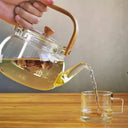 Chaleira de vidro 1L com infusor e alça de bambu natural, servida com chá em ambiente aconchegante - Casa Splêndida