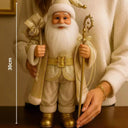 Boneco de papai noel dourado com tamanho de 30cm sob uma mesa com uma mulher atrás o segurando.