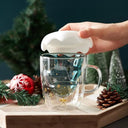Caneca de Natal Casa Splendida de vidro transparente, com bebida quente e mini enfeites natalinos sobre a mesa