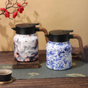Garrafa térmica estampada em cerâmica, modelos azul floral e marmorizado, sobre mesa posta com xícara