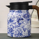 Garrafa térmica azul floral com tampa preta e alça amadeirada, vista frontal em fundo claro