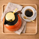 Garrafa Térmica Luxo Valenza para Café e Chá 1L Laranja Casa Splendida sendo visto de cima sob uma bancada ao lado de uma xícara de café