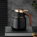 Garrafa térmica preta com detalhes dourados e alça amadeirada em bancada escura, ambiente moderno