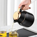 Mão servindo café da garrafa térmica preta com tampa dourada, bebida sendo despejada no copo