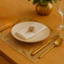 ogo americano retangular dourado com textura vazada em mesa posta minimalista com prato e taça transparentes.