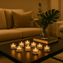 Castiçais de vidro com velas acesas em ambiente de sala, compondo decoração acolhedora ao lado de livros e plantas.