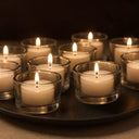 Conjunto de castiçais de vidro baixo com várias velas acesas, produzindo iluminação suave e elegante para ambientes internos.