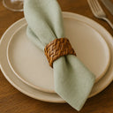 Detalhe do anel de guardanapo em rattan claro com trançado artesanal rústico, aplicado em guardanapo verde