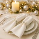 Anel para guardanapo com pérolas duplas aplicado em guardanapo dobrado sobre prato claro, composição refinada para mesa posta