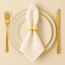 Anel de guardanapo com pérola dupla em composição clean com louça clara e talheres dourados, mesa posta sofisticada