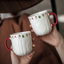 Caneca de cerâmica natalina sobre mesa decorada, destacando a borda com símbolos de Natal