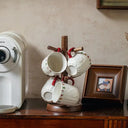 Quatro canecas de cerâmica com detalhes natalinos penduradas em ganchos decorativos na cozinha