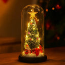 Luminária de Mesa de Natal com Árvore e Luz LED Casa Splendida acesa à noite, emitindo brilho dourado sob cúpula de vidro e base de madeira natural.