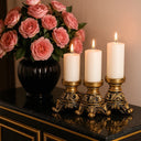 Trio de castiçais dourados coloniais expostos sobre bandeja decorativa com arranjo floral rosa, estilo luxuoso.