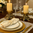 Par de castiçais dourados estilo europeu com acabamento vintage, decorados com vela alta sobre mesa clássica.