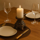 Composição refinada com castiçais dourados, pratos brancos e taças transparentes em mesa de jantar luxuosa.