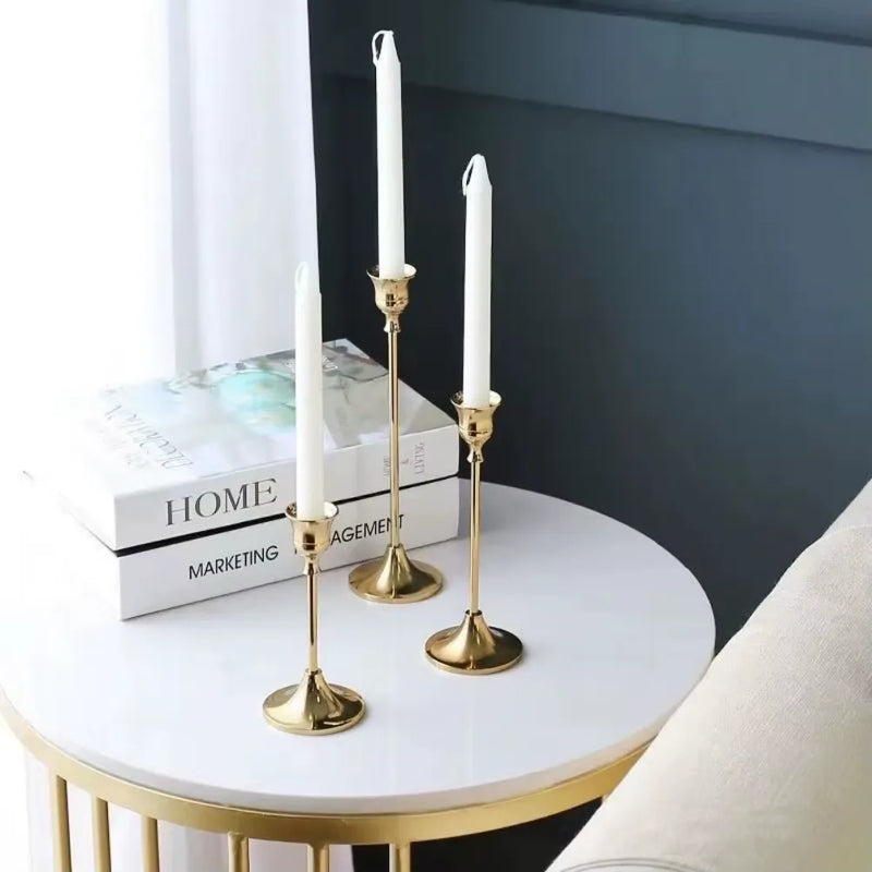 Kit 3 castiçais vintage dourados em alturas diferentes sobre mesa decorada”
