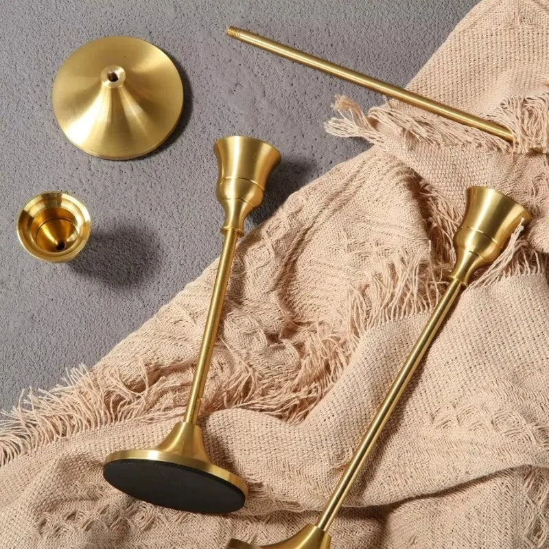 Kit 3 castiçais vintage dourados em alturas diferentes sobre mesa decorada”