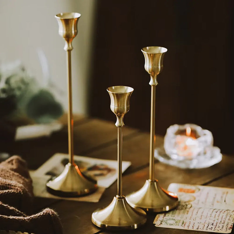 Kit 3 castiçais vintage dourados em alturas diferentes sobre mesa decorada”