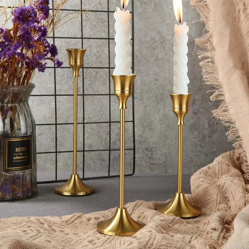 Kit 3 castiçais vintage dourados em alturas diferentes sobre mesa decorada”