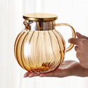 Bule de vidro transparente com tampa dourada e infusor interno, ideal para chás e infusões, sobre mesa de madeira