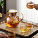 Bule de vidro transparente com tampa dourada e infusor interno, ideal para chás e infusões, sobre mesa de madeira