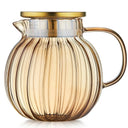 Bule de vidro transparente com tampa dourada e infusor interno, ideal para chás e infusões, sobre mesa de madeira