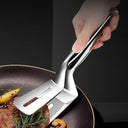 Pinça 3-em-1 em aço inox segurando e virando bife na frigideira – Casa Splendida